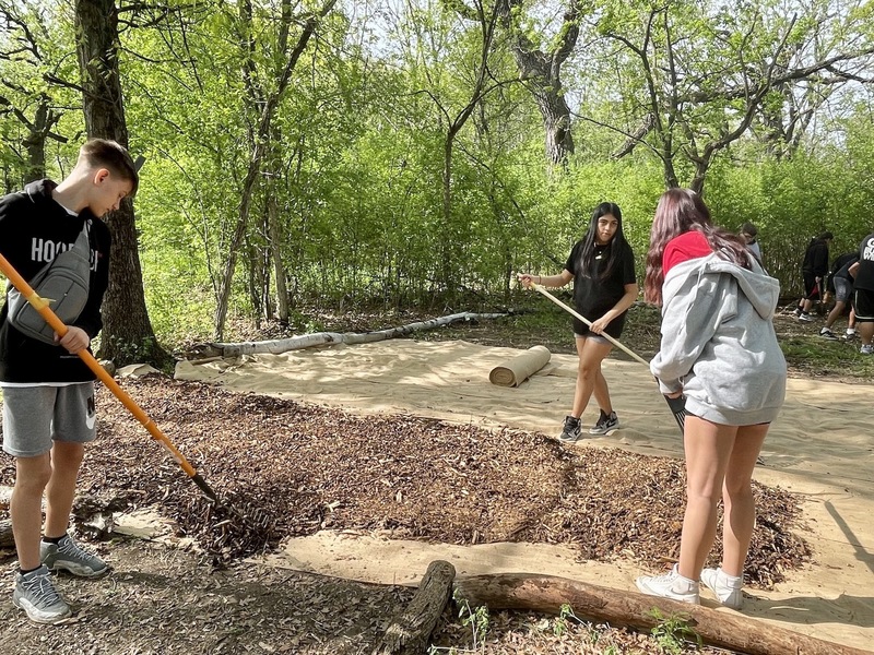 Three students spread mulch over weed barrier.