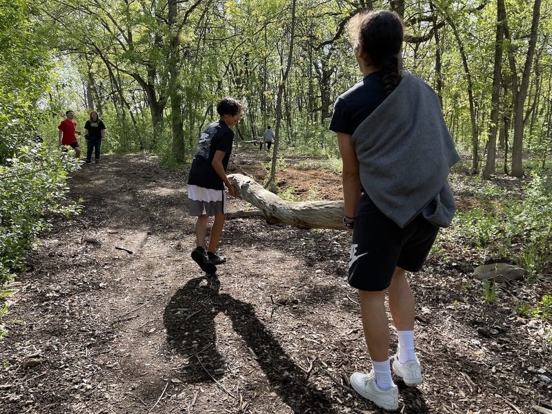 Two students carrying a large log through the woods.